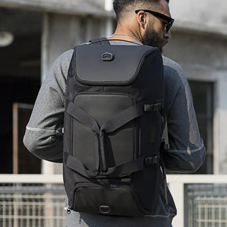Man wearing a black backpack with a brand logo, standing outdoors.