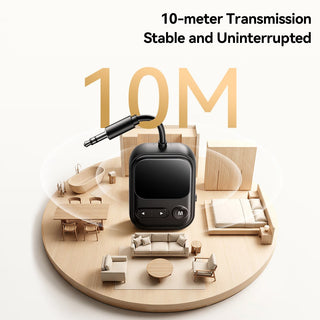 A small black electronic device with a 3.5mm jack cable is centered on a circular wooden display base, surrounded by miniature room props like a sofa, bed, table, and bathtub.