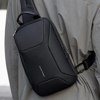 A black sling bag with a silver 'mark Ryden' logo, worn crossbody on a person wearing a gray jacket.