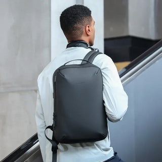 Man with sleek black minimalist backpack on escalator, tech travel accessory