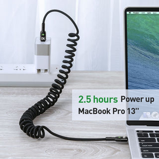 Coiled charging cable with power adapter next to a MacBook Pro on a desk.