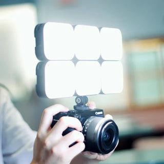 Person holding a Canon camera with a light panel in front of a blurred background